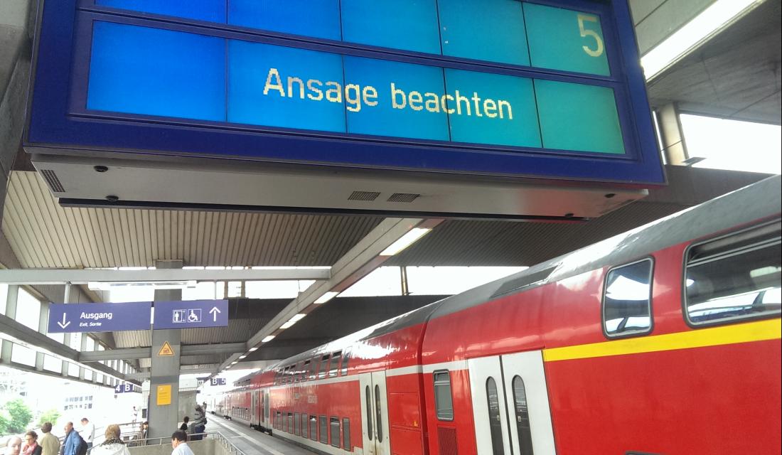 Ein doppelstöckiger Regionalzug steht an einem Bahnhofsgleis, auf der Anzeige steht: "Ansage beachten"