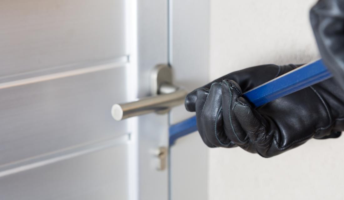 Ein Einbrecher versucht mit einer Brechstange eine Tür zu öffnen.