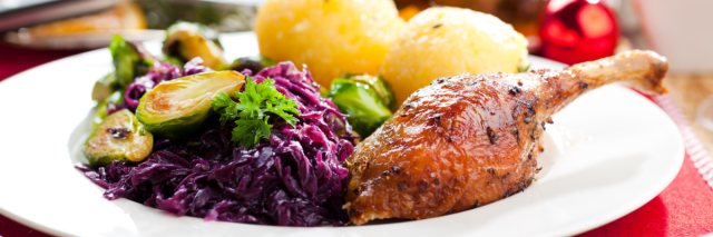 Auf einem Festtagstisch steht ein Teller mit Enten-Keule, Knödeln und Rotkohl