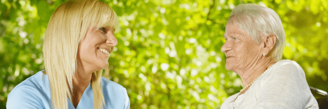 Eine Pflegerin sitzt mit einer älteren Dame draußen und hält ihre Hand.