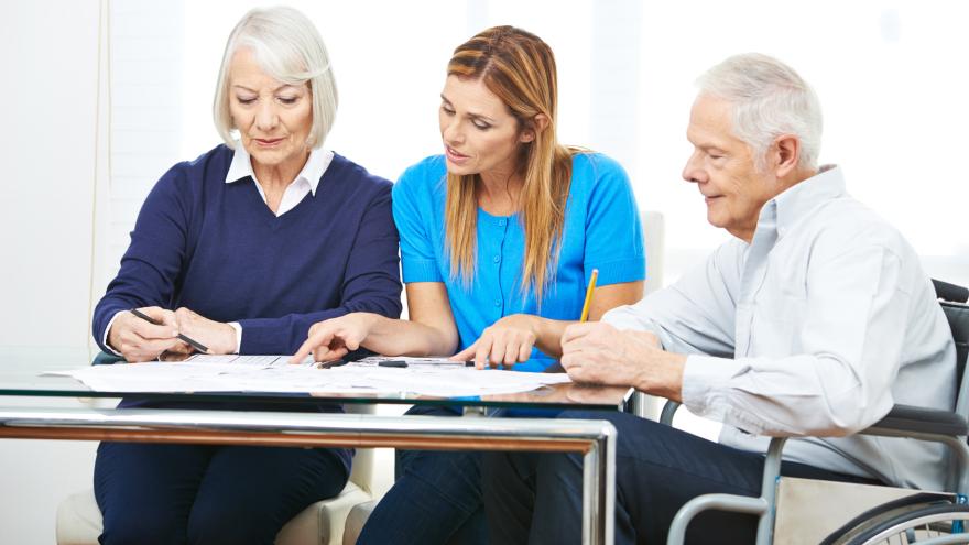 Senioren schauen sich in einem Pflegeheim mit einer Betreuerin einen Vertrag an.