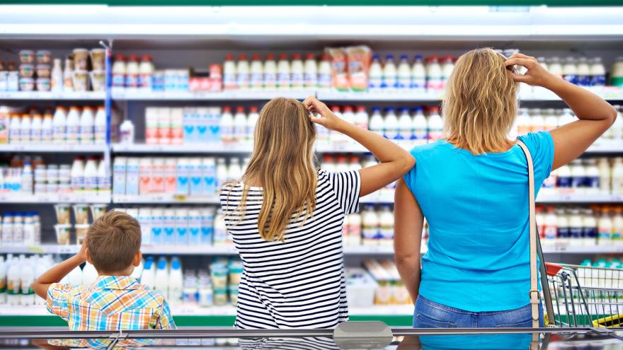 Eine Familie steht im Supermarkt und schaut auf die mit Lebensmitteln gefüllten Regale.