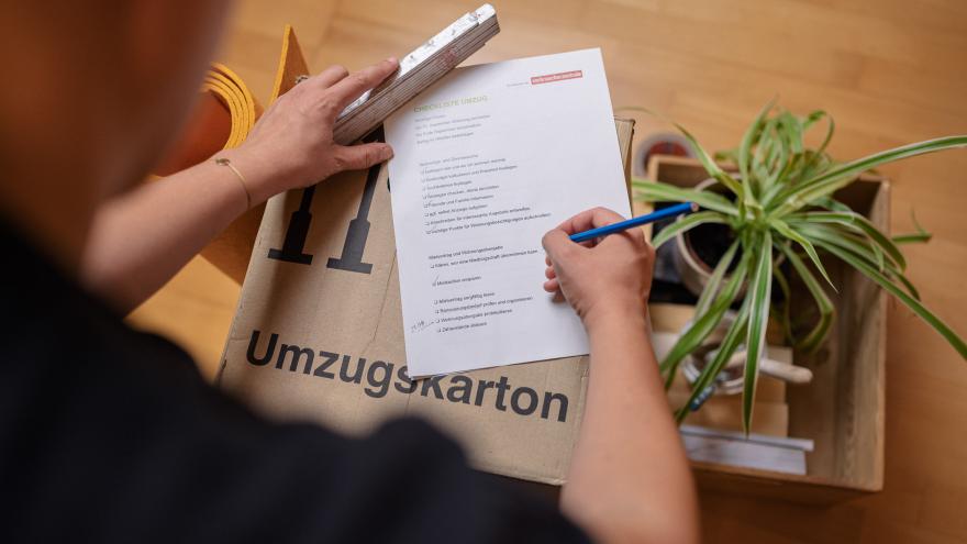 Mann hakt Umzugs-Checkliste auf Umzugskarton ab