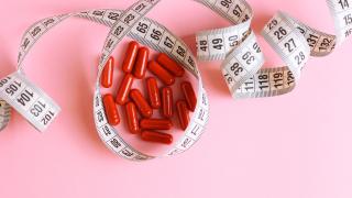 Rote Abnehmtabletten liegen auf einem Tisch, umschlossen von einem Maßband