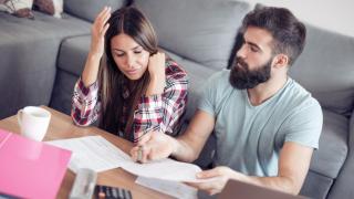 Ein Paar sitzt vor dem Wohnzimmertisch mit Finanzunterlagen und ist unzufrieden